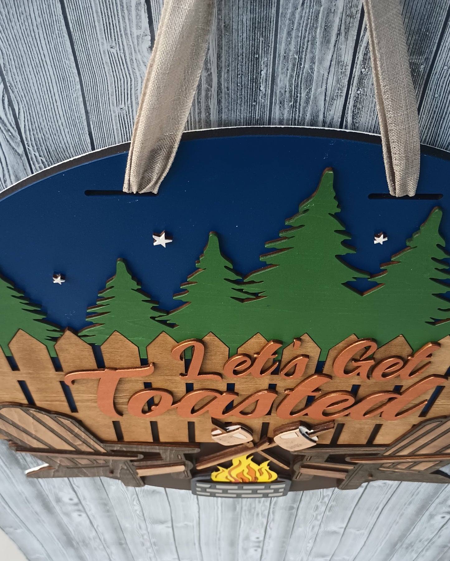 Campfire-themed door hanger for outdoor enthusiasts with rustic fence and pine tree accents.