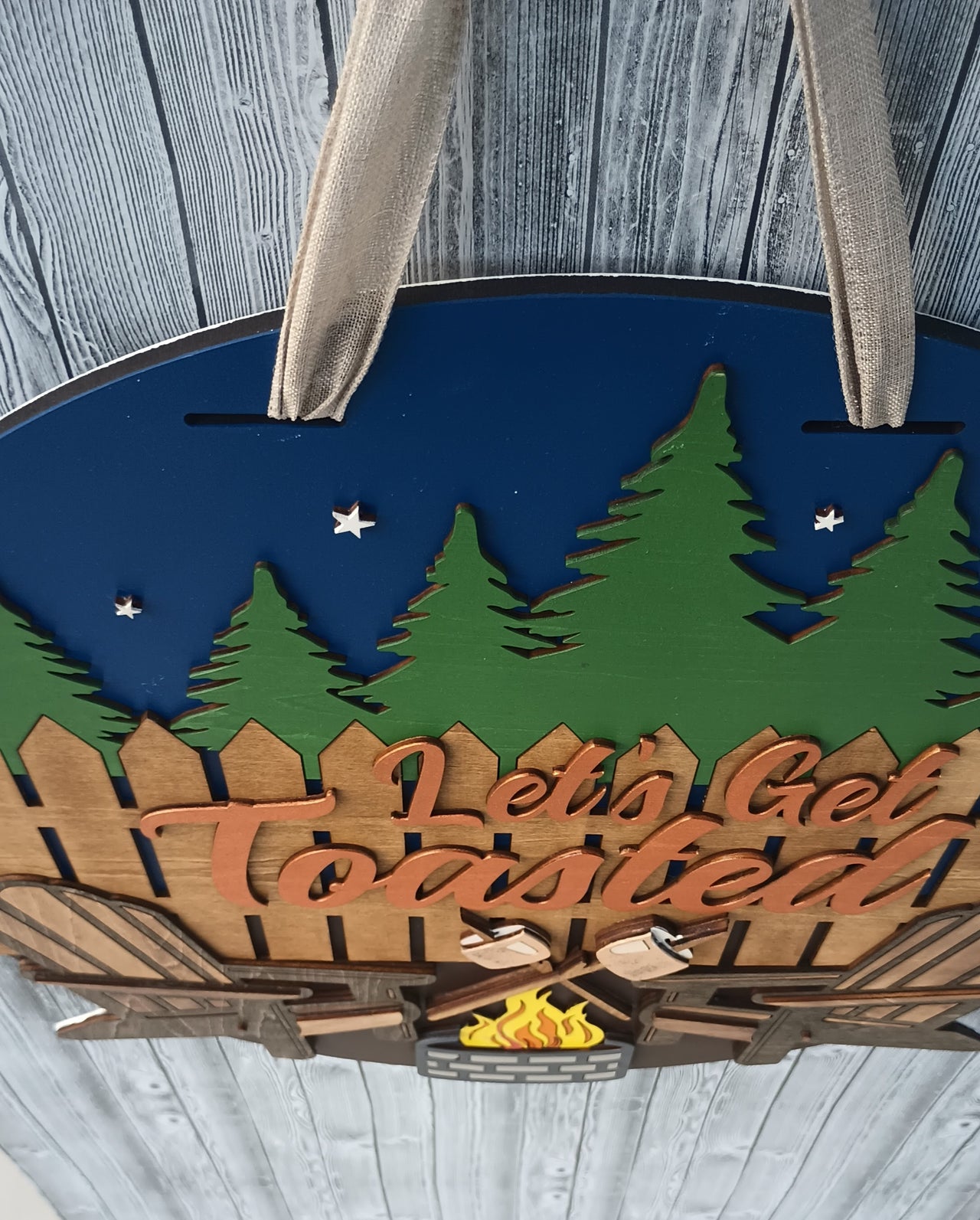Campfire-themed door hanger for outdoor enthusiasts with rustic fence and pine tree accents.