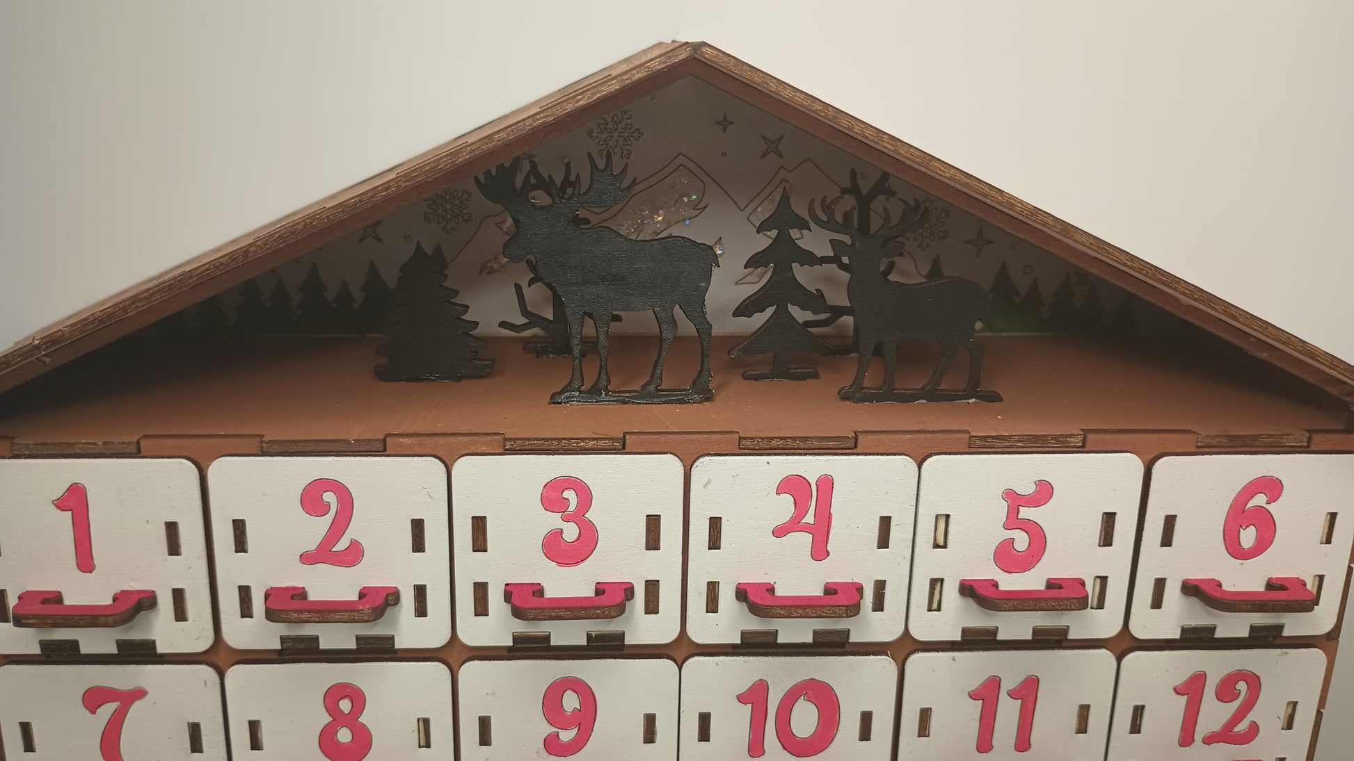 Top decorative detail of a wooden advent calendar, showcasing festive trees and reindeer silhouette design.