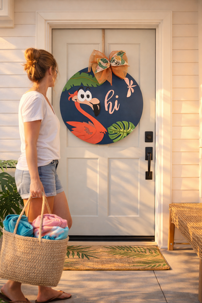 Woman standing outside a house with a decorative flamingo door sign on the door.