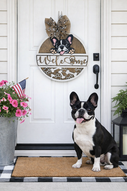 French bulldog standing on a doormat in front of a door with a decorative wooden front door sign featuring a french bulldog dog design.

