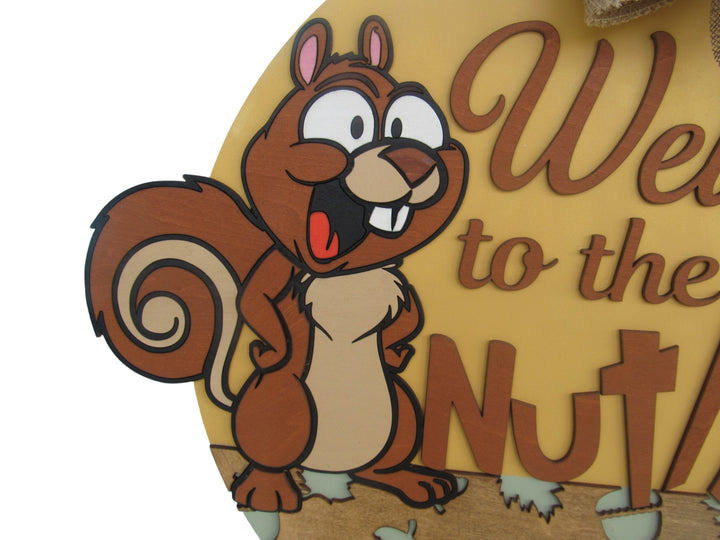 Woodland-themed round door hanger featuring a happy squirrel and layered acorn graphics with sunflower ribbon bow.
