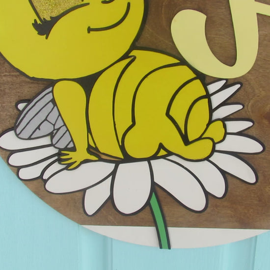Bee-themed wooden door hanger with “Hi” greeting and sunflower bow displayed on a light blue front door