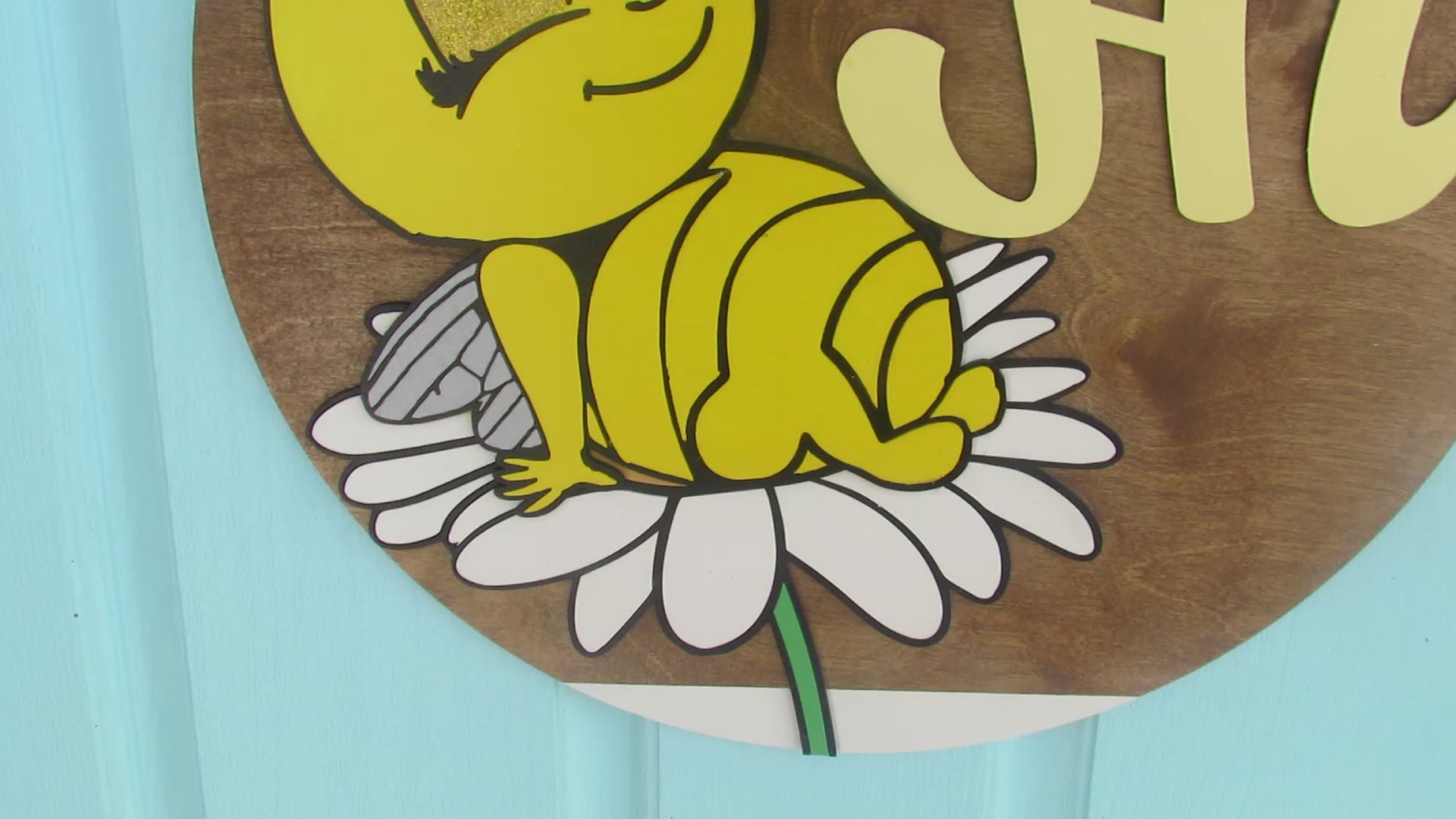 Bee-themed wooden door hanger with “Hi” greeting and sunflower bow displayed on a light blue front door