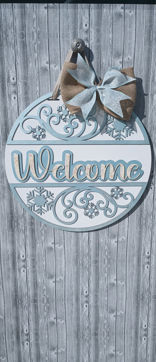 Welcome Winter door hanger with hand-painted snowflake accents, burlap bow, and frosty blue swirl design, perfect for winter front door décor.