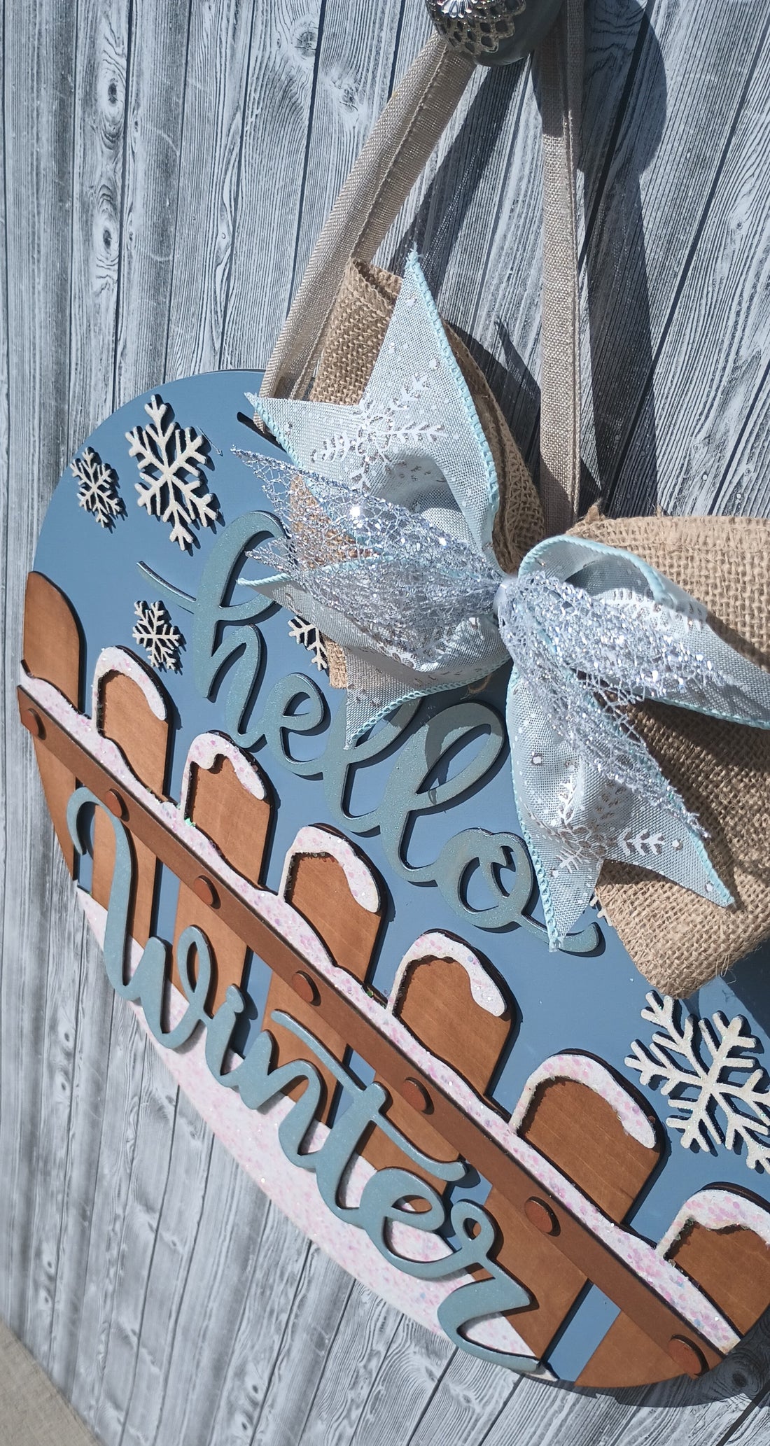 Winter door hanger featuring glitter, snowflake designs, and a burlap bow charm on an 18-inch round wooden base for winter decor.